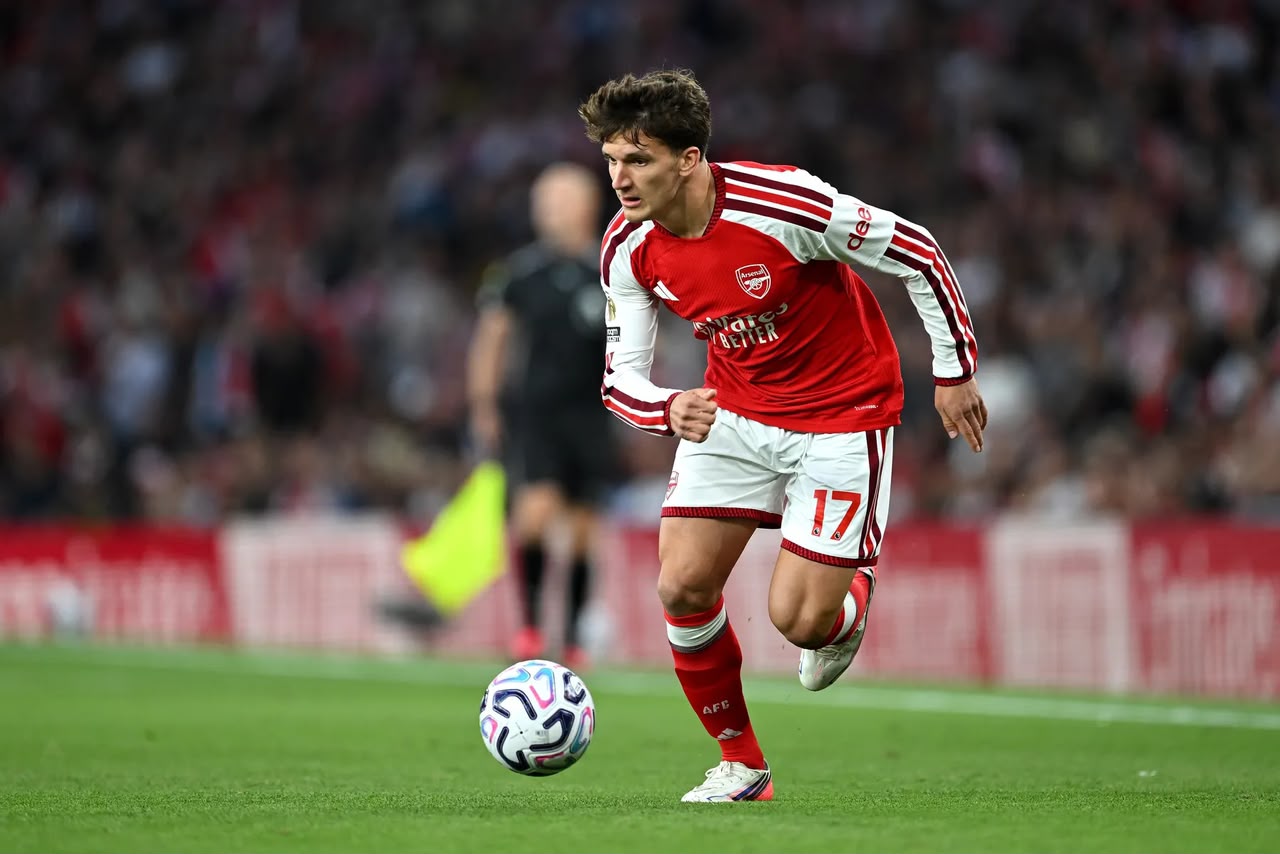 Christos Tzolis wearing a red and white Arsenal home kit with the number 17 on his shorts, running forward with a football at his feet during a match