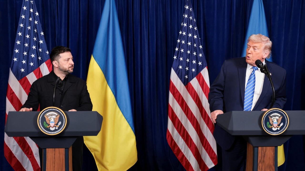 Ukrainian President Volodymyr Zelenskyy and Donald Trump stand at matching podiums in front of US and Ukrainian flags during a press briefing.