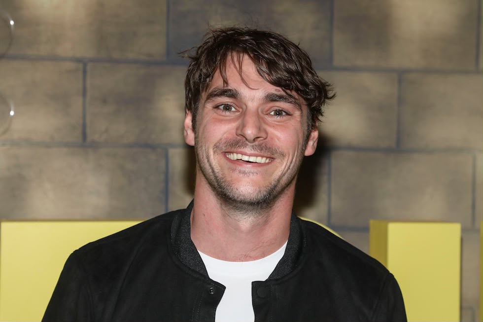 Actor RJ Mitte smiling while posing against a bright yellow background featuring an Apple TV+ logo.